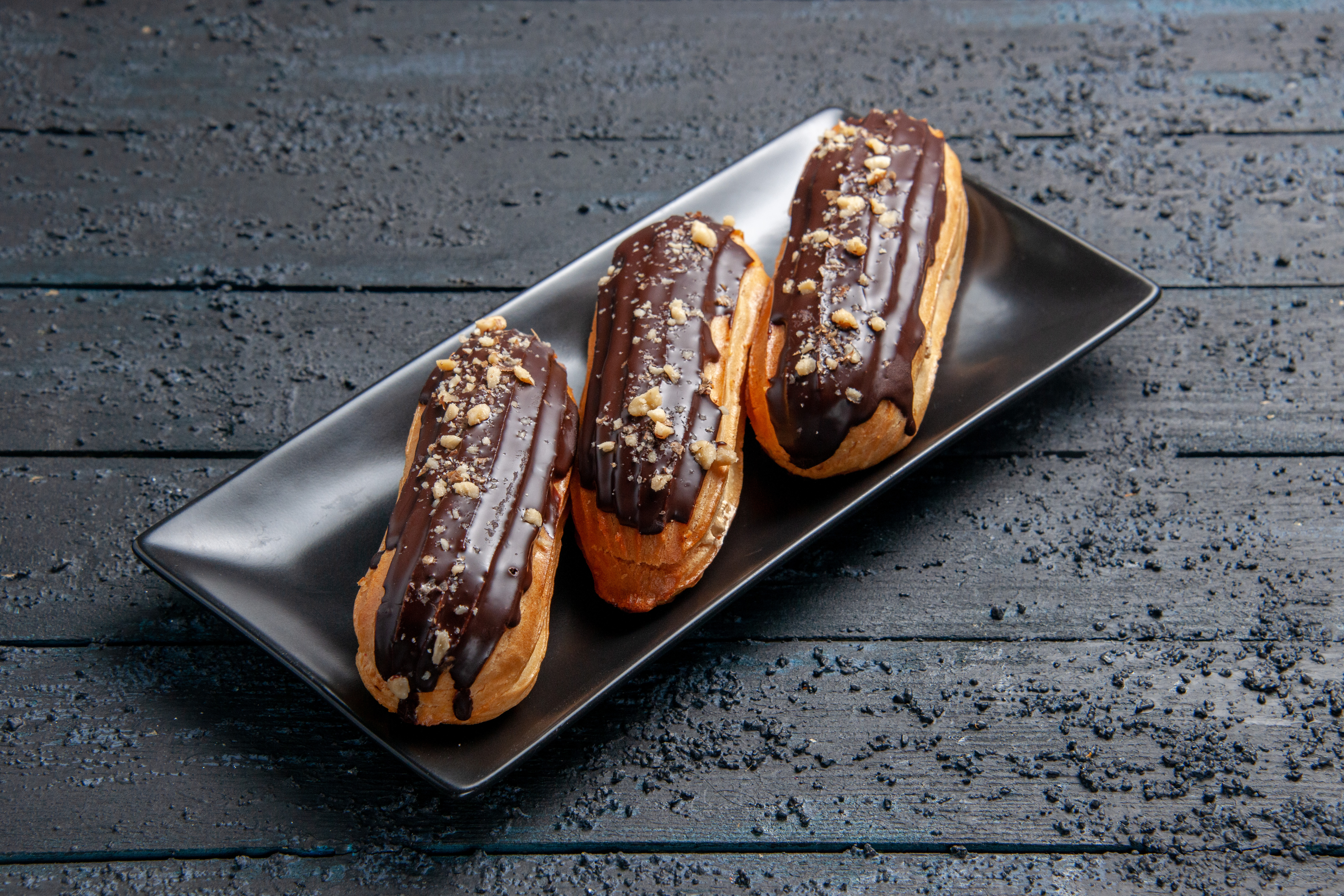 eclairs-de-chocolate-em-uma-placa-retangular-na-mesa-de-madeira-escura-com-espaco-livre.jpg